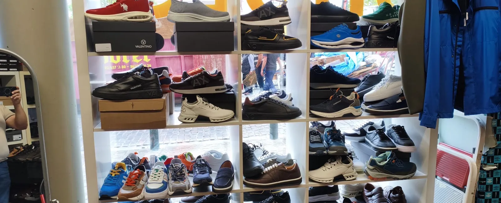 Wall of sneakers arranged by compartment, with Valentino boxes visible, at Outlet Chaussures Bruxelles, Place du Jeu de Balle