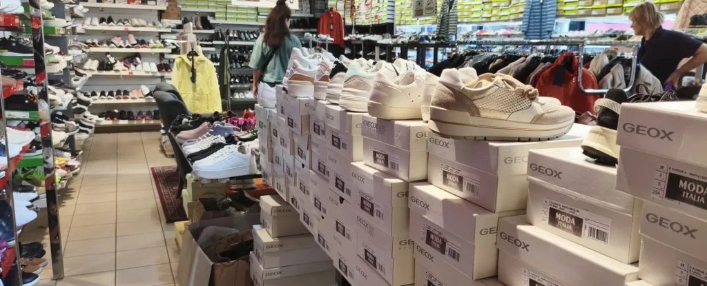 Long row of Geox boxes topped with white sneakers in the aisle of Outlet Chaussures Bruxelles, Place du Jeu de Balle